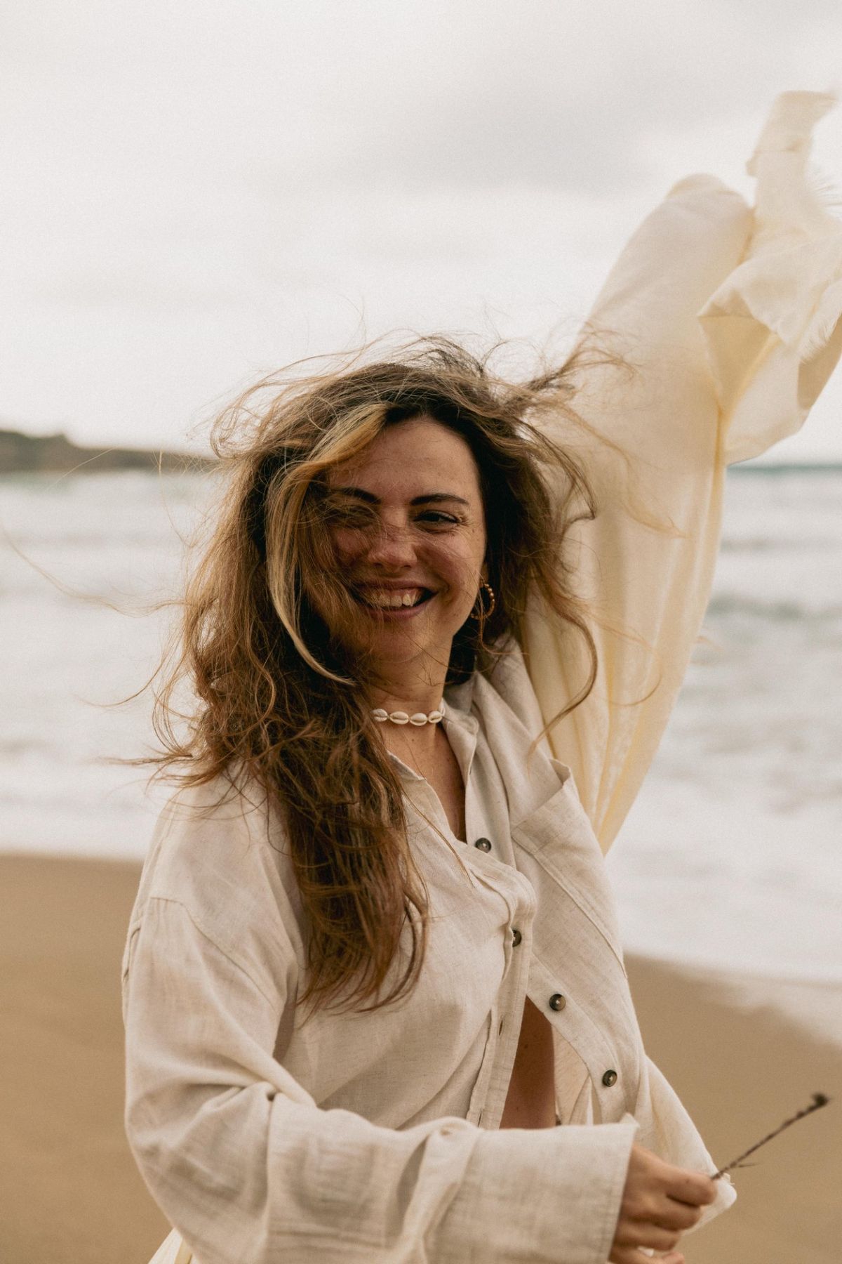 Lucia standing on rocks by the sea, arms raised to the sky