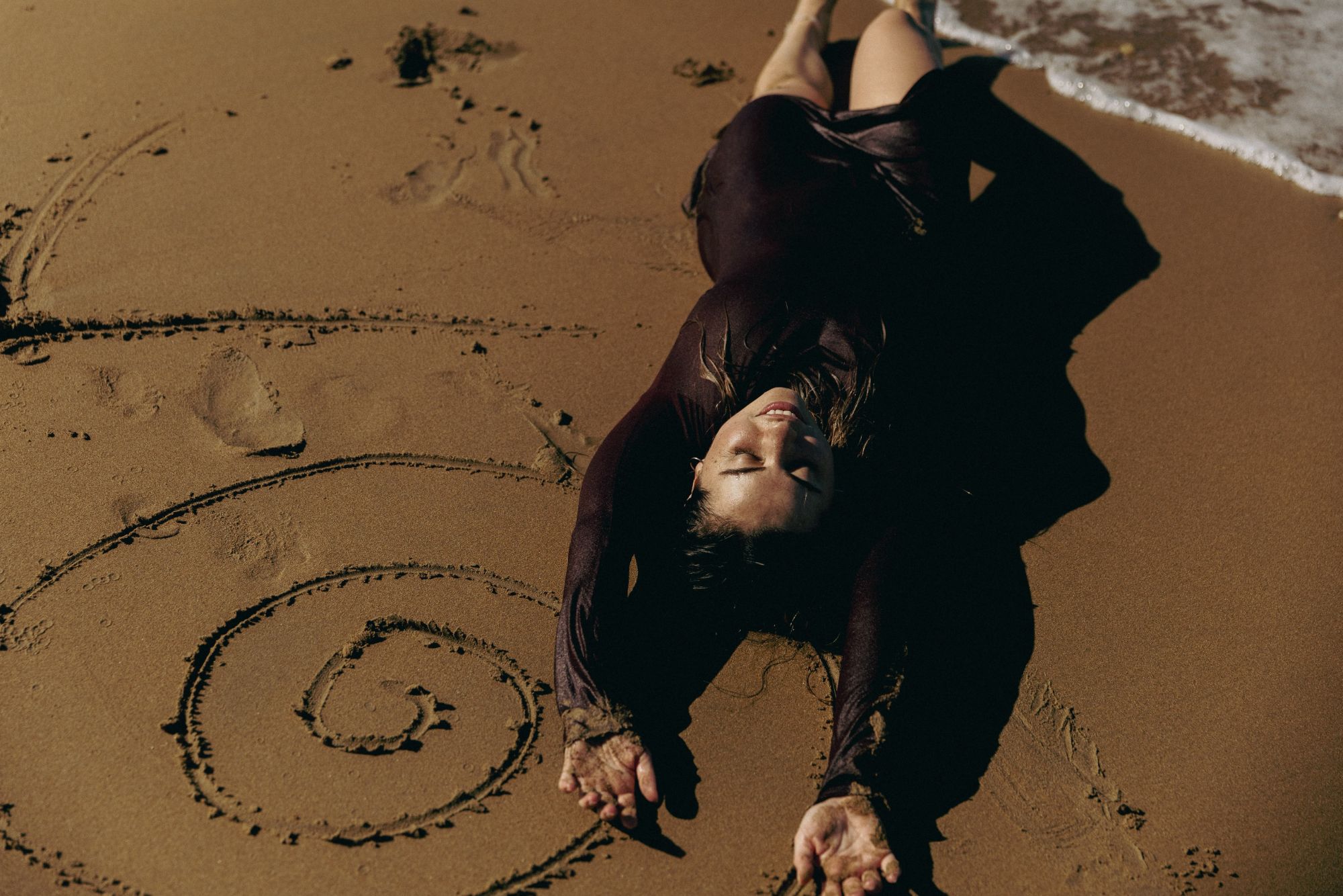 Lucia lying in the sand beside a spiral she drew, eyes closed